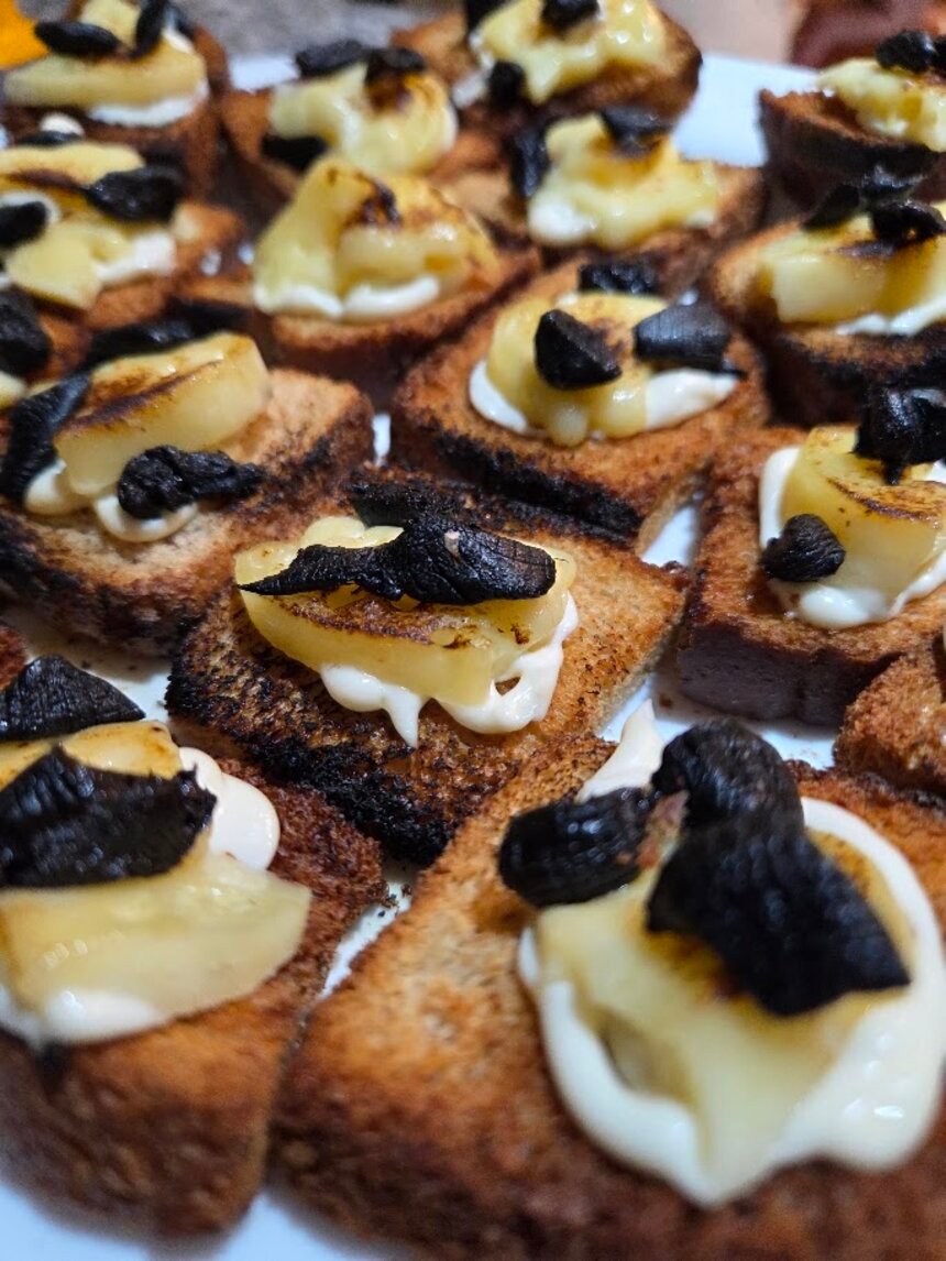 Canapés de pão torrado com queijo e lâminas de alho negro por cima